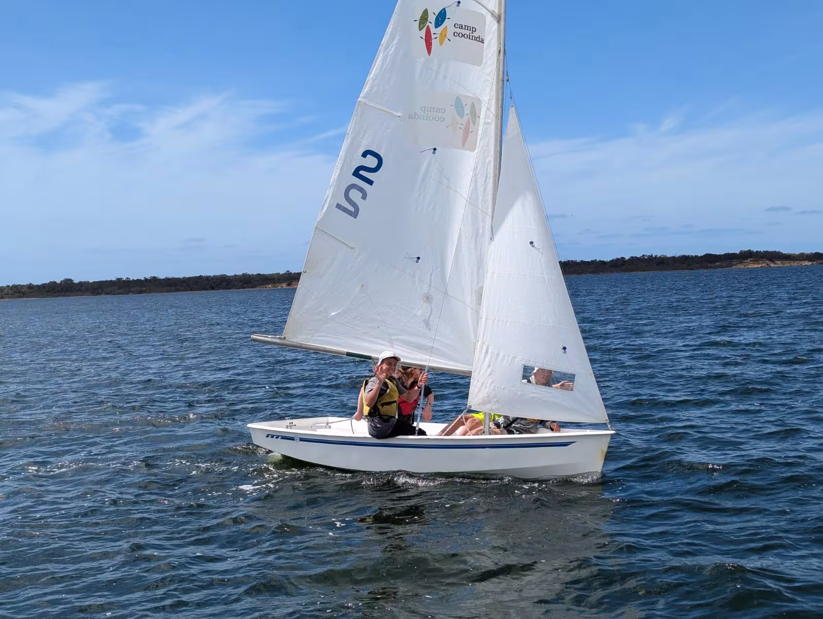 A white sailing boat floating on the Gippsland Lakes with waving young people