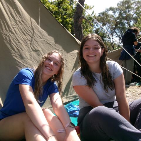 Two smiling campers sitting in front of a tent