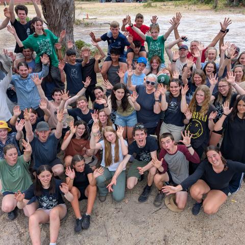 A group of campers standing together looking up at the camera with hands raised in jubilation