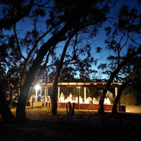 Nightime view of the main dining area from a distance with lights on a people sitting at tables
